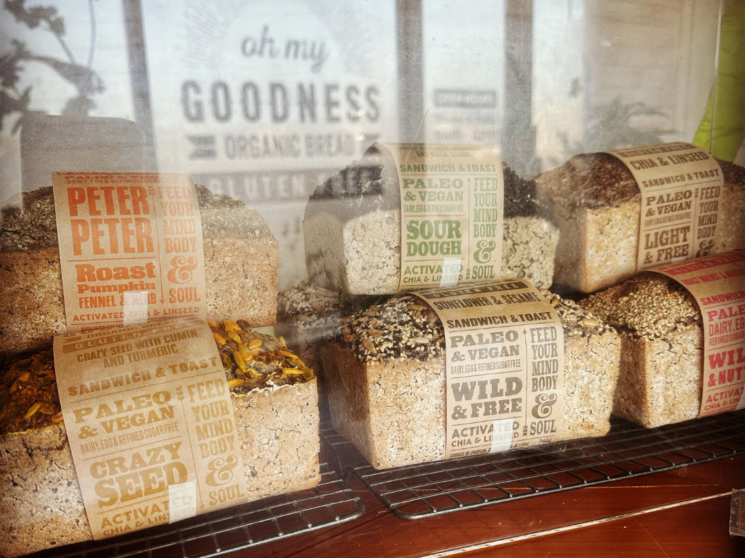 Loaves of freshly baked OMGoodness bread with the OMG Organic & Gluten Free window signage reflected in the background