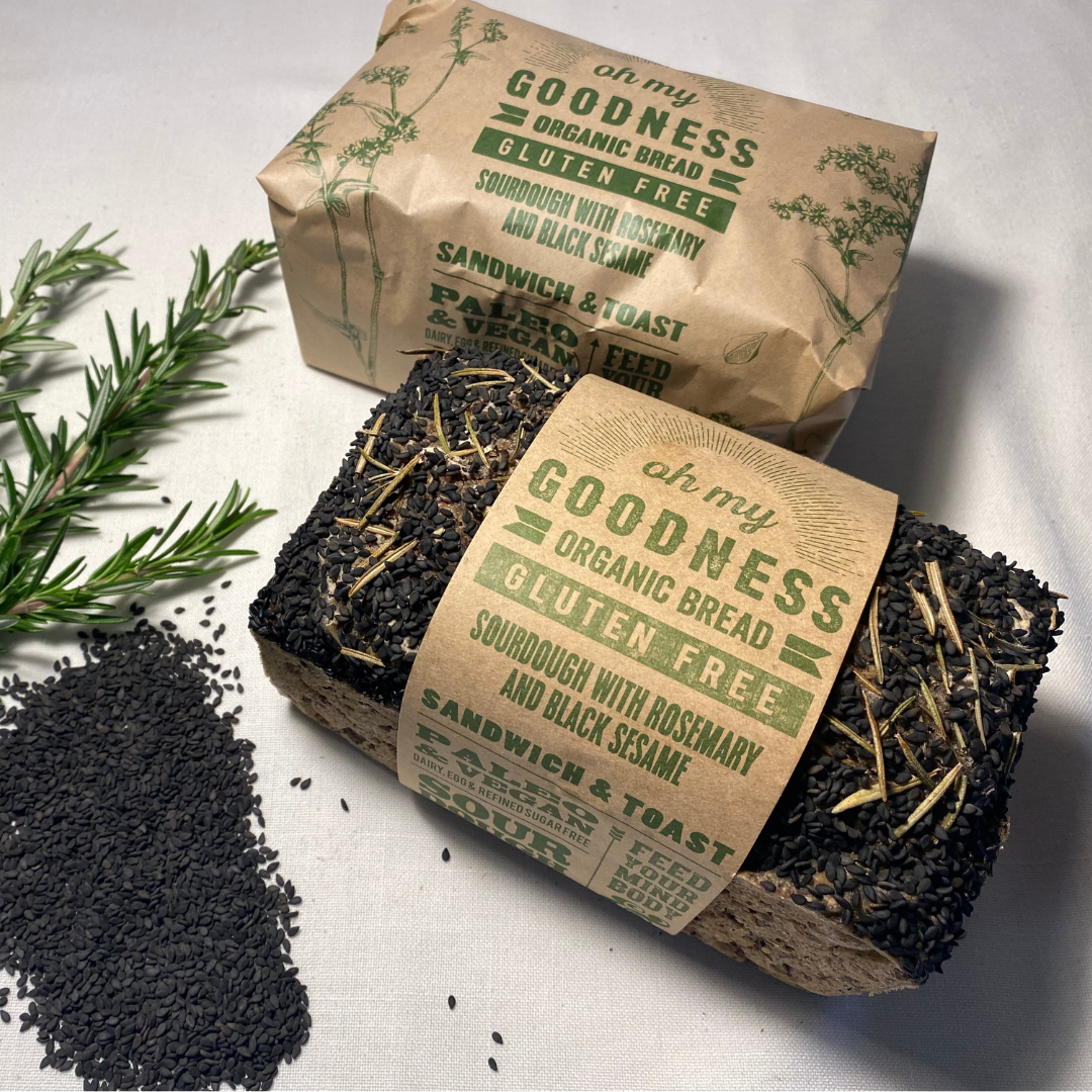 OMGoodness Sourdough w/ Rosemary & Black Sesame GF Organic loaf of bread on a white background with fresh rosemary & black sesame seeds sprinkled alongside. Label reads Gluten Free, Paleo & Vegan, Dairy, Egg & Refined Sugar Free