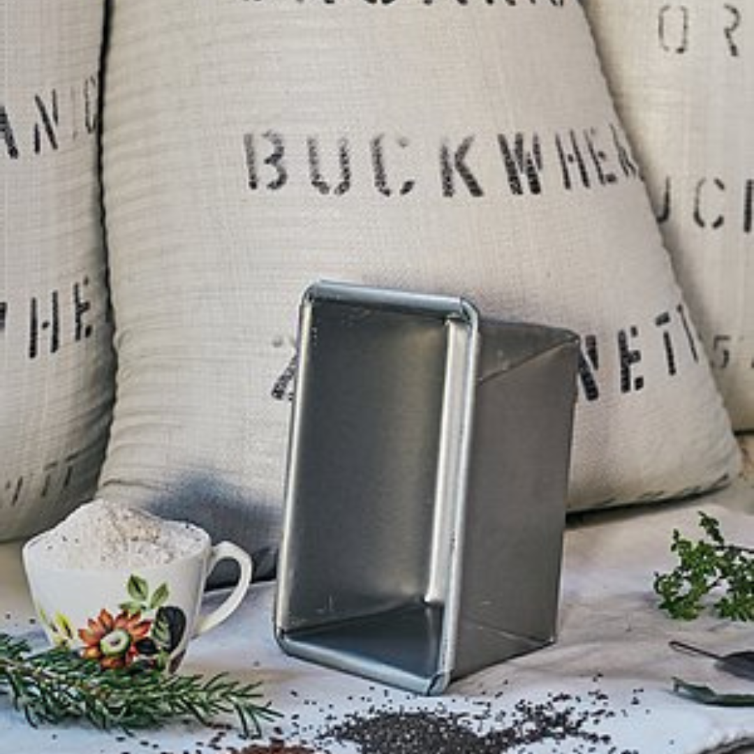 Commercial bread tin, perfect for baking OMGoodness GF/DF Organic bread, standing on it&#39;s short edge in front of a sack of organic buckwheat flour with rosemary and dried herbs