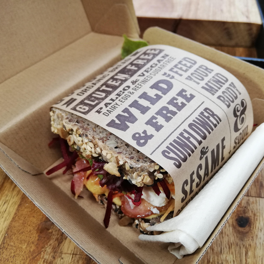 Fresh salad sandwich made with OMGoodness Sunflower &amp; Sesame &#39;Wild &amp; Free&#39; GF Organic loaf of bread wrapped in product label which reads Gluten Free, Paleo &amp; Vegan, Dairy, Egg &amp; Refined Sugar Free