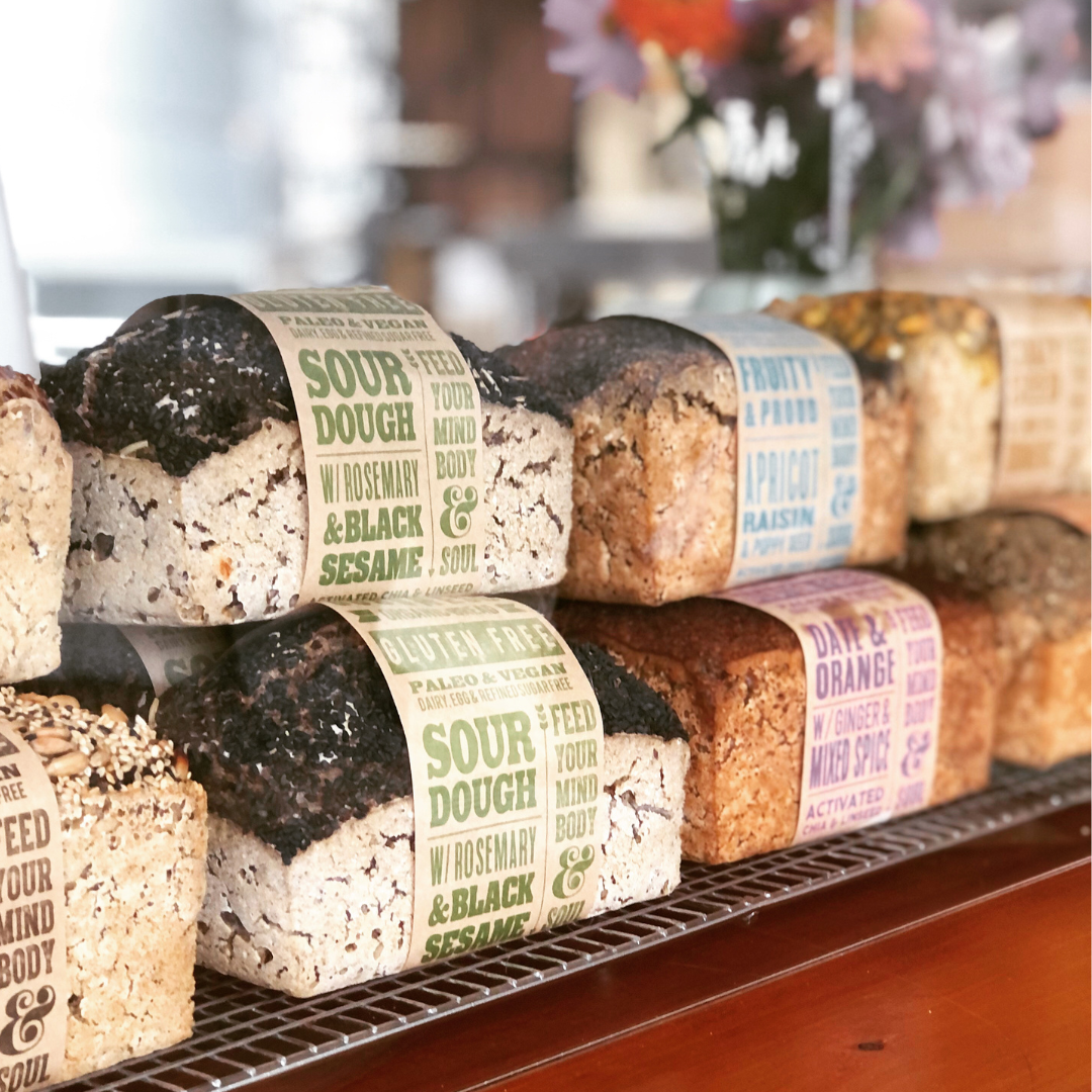 OMGoodness Sourdough w/ Rosemary &amp; Black Sesame GF Organic loaves of bread in a display with other OMG loaves. Label reads Gluten Free, Paleo &amp; Vegan, Dairy, Egg &amp; Refined Sugar Free
