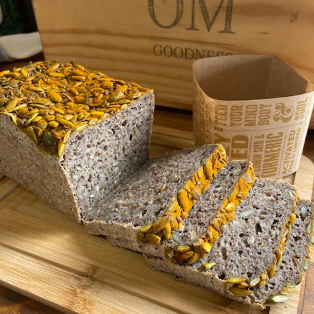OMGoodness 'Crazy Seed' with Cumin & Turmeric GF Organic loaf of bread on a white background with pumpkin seeds, sunflower seed, cumin seeds, linseeds, turmeric powder & fresh rosemary sprinkled below. Label reads Gluten Free, Paleo & Vegan, Dairy, Egg & Refined Sugar Free