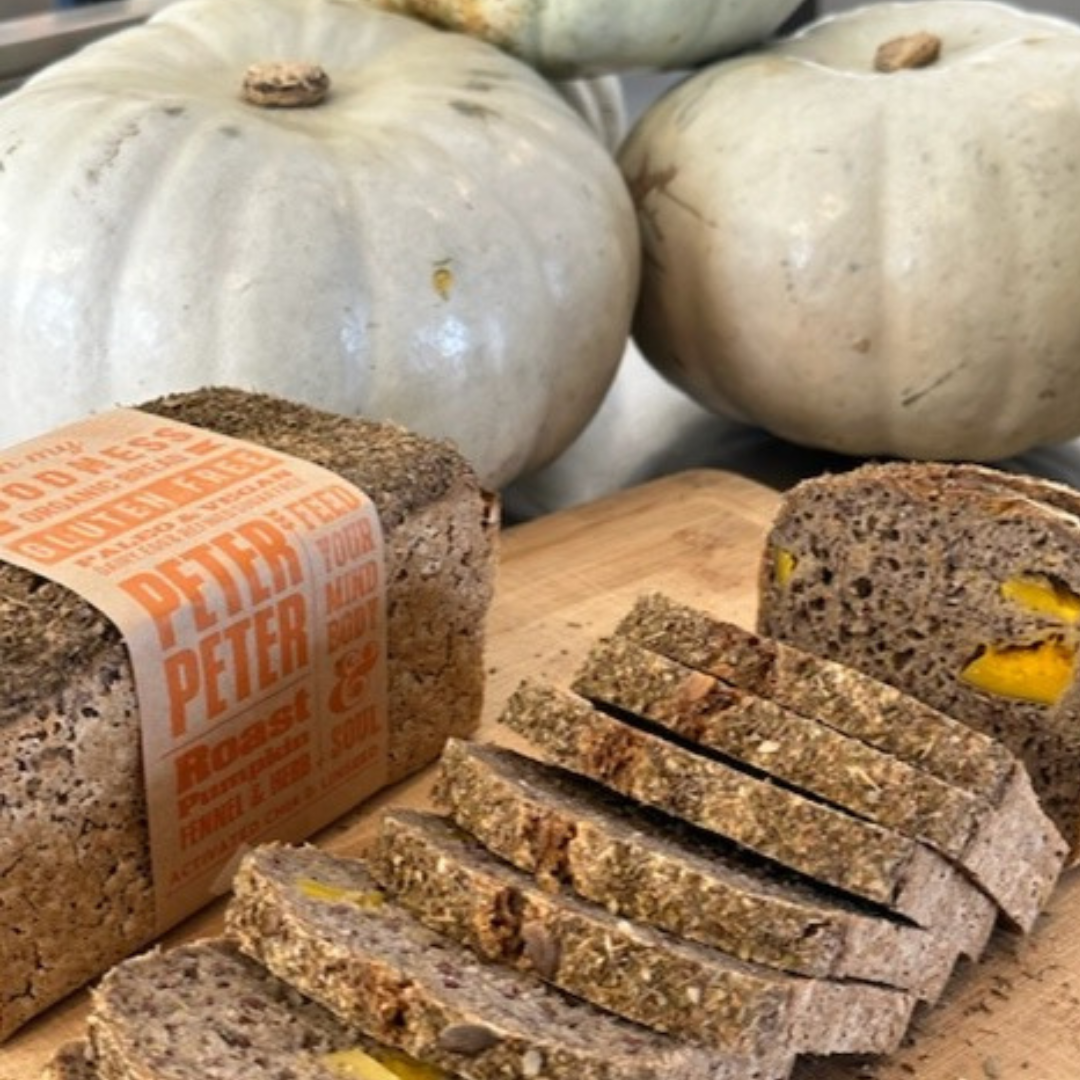OMGoodness Roast Pumpkin, Fennel & Herb 'Peter, Peter' GF Organic loaf of bread on a white background with fresh rosemary, fennel seeds, pumpkin seeds & mixed herbs sprinkled below. Label reads Gluten Free, Paleo & Vegan, Dairy, Egg & Refined Sugar Free
