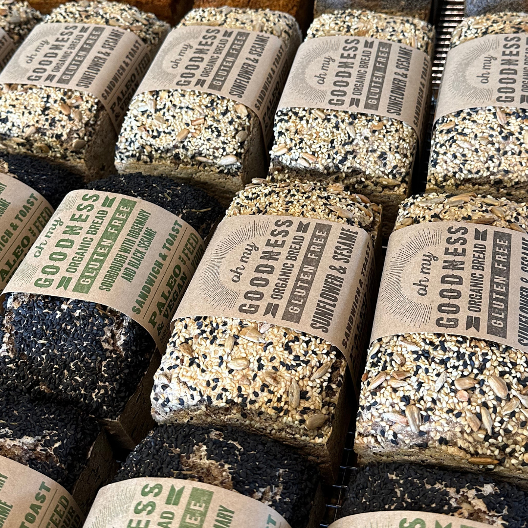 OMGoodness Sunflower & Sesame 'Wild & Free' GF Organic loaves lined up on baking table. Label reads Organic Bread, Gluten Free, Sandwich & Toast