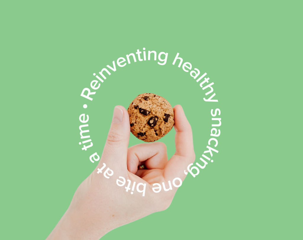 Wisefoods | hand holding an allergen friendly Dark Choc Chip Wise Cookie, encircled by the words "Reinventing healthy snacking, one bite at a time" on a green background