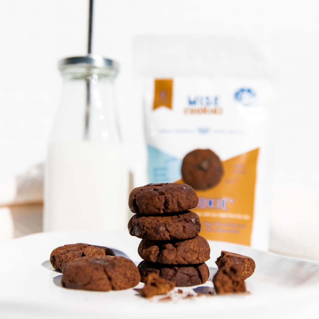 Wisefoods | 4.5 Health Star rated, allergy-friendly Double Choc &quot;Brookie&quot; Wise Cookies on a white plate with a bottle of plant based milk &amp; Snack Pack out of focus in the background 
