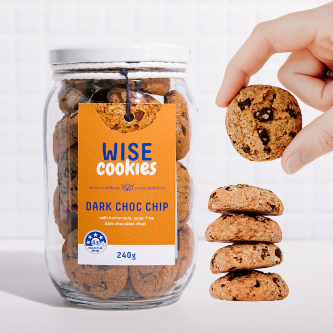 Wisefoods | 4.5 Health Star rated, allergy-friendly, plant based Dark Choc Chip Wise Cookies in a glass jar with a stack of loose cookies and a hand holding one between thumb and forefinger to the right of the jar