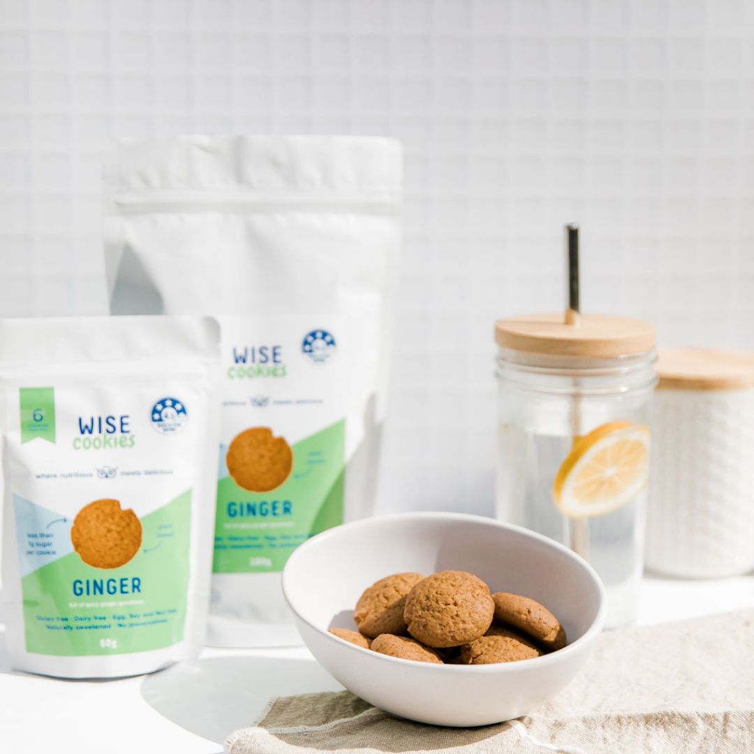Wisefoods | Snack Pack and Pantry Pack of 4.5 Health Star rated, allergy-friendly and plant based Ginger Wise Cookies, displayed with a small white bowl of Ginger cookies and a sipping glass of lemon water against a white backgound