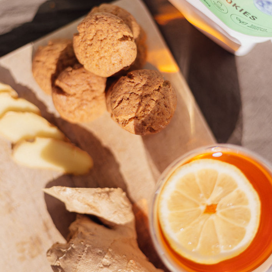 Wisefoods | 4.5 Health Star rated, allergen-friendly and plant based Ginger Wise Cookies on a wooden chopping board with slices of fresh ginger and a lemon slice on black tea alongside