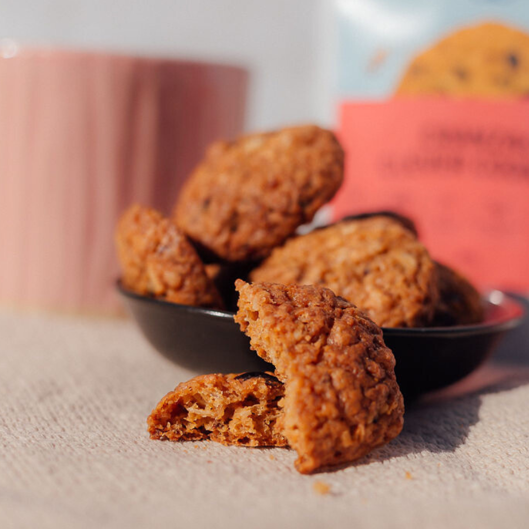 Wisefoods | Cranberry 4.0 Health Star rated &amp; allergen-friendly cookies loose on a pale table mat with an out of focus rose-coloured cup and a Snack Pack in the background