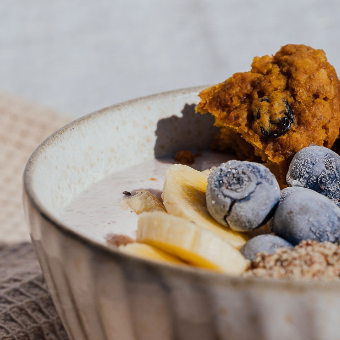 Wisefoods | Close up of a breakfast bowl topped with sliced banana, frozen blueberries and crumbled 4.0 Health Star rated and allergy-friendly, low sugar Fruit &amp; Spice collagen Wise Cookies