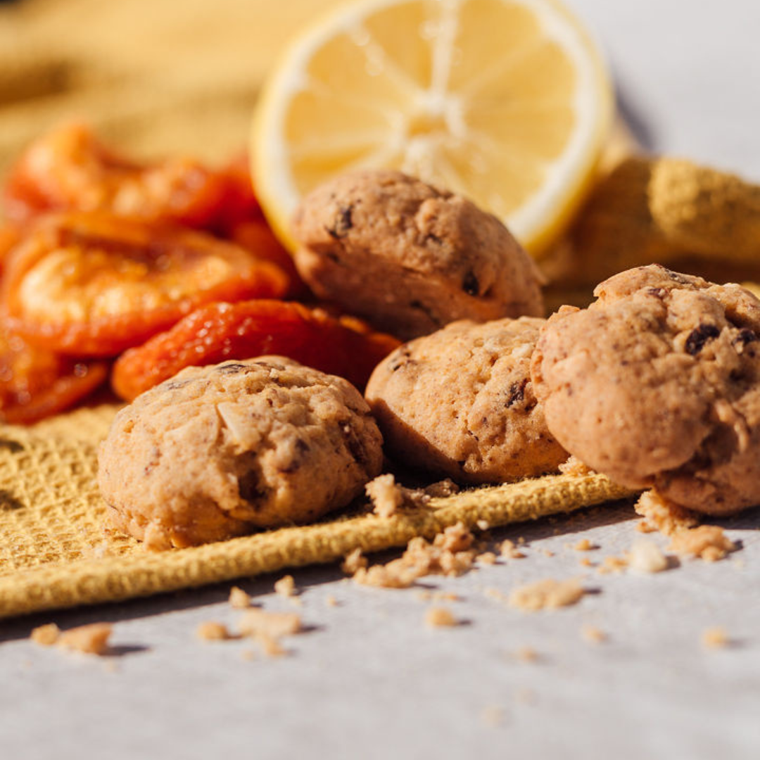 Wisefoods | 4.0 Health Star rated and allergen-friendly Apricot &amp; Lemon Cookies &amp; crumbs on a light-mustard-coloured table mat with dried apricots and cut fresh lemon in the background